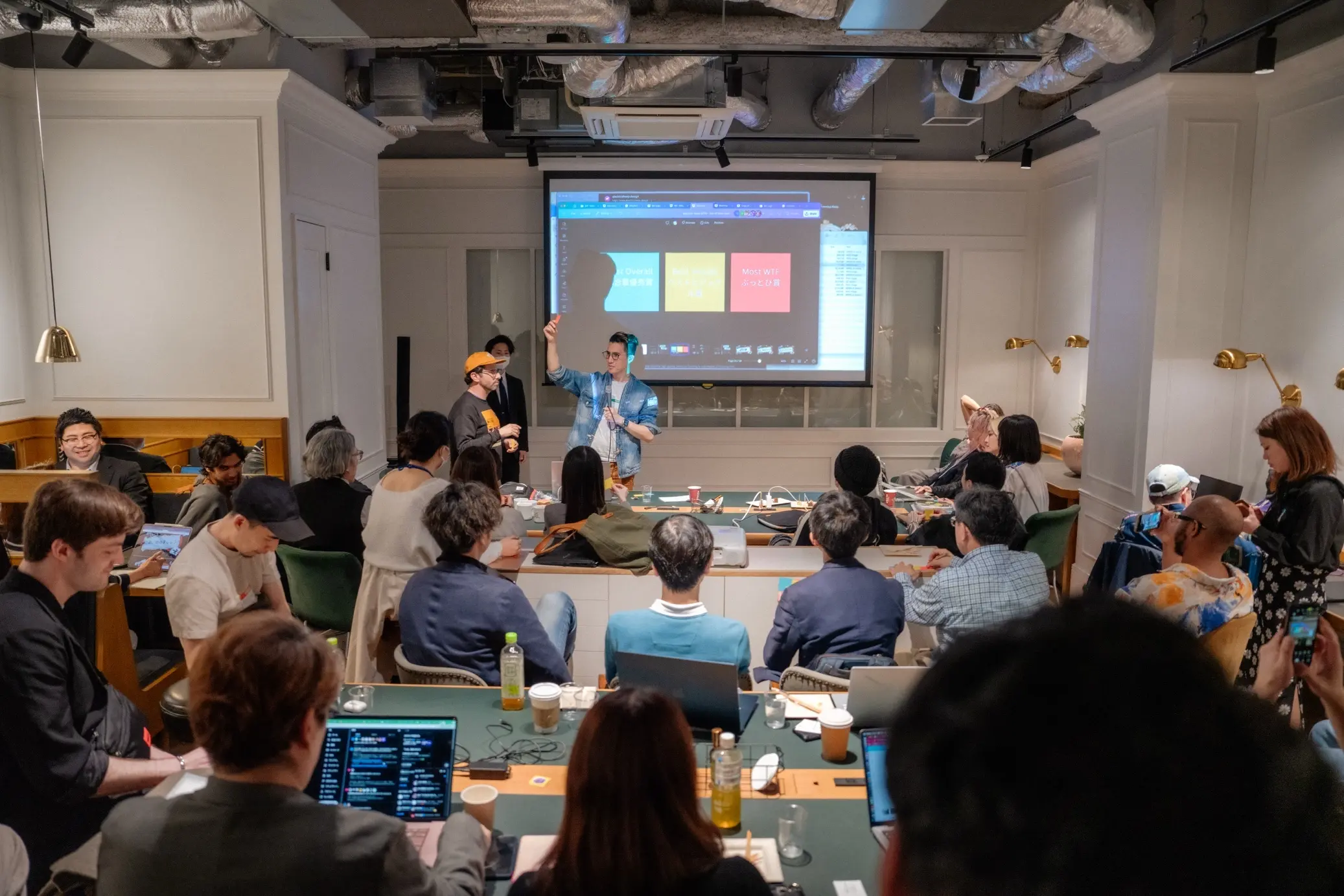 Machine Cinema GenJam workshop showcase — presenters at the front of a packed room, prize categories on the projector behind them.