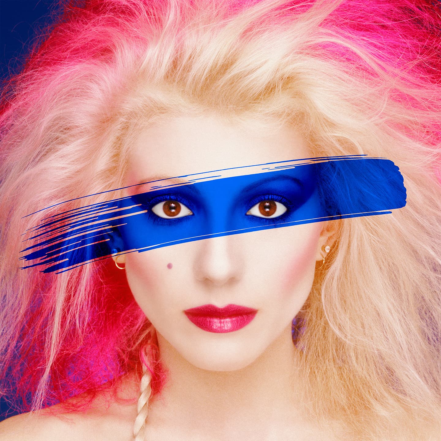 Studio portrait of a woman with platinum and hot-pink teased hair and a broad cobalt-blue brushstroke painted across her eyes, against a blue ground.