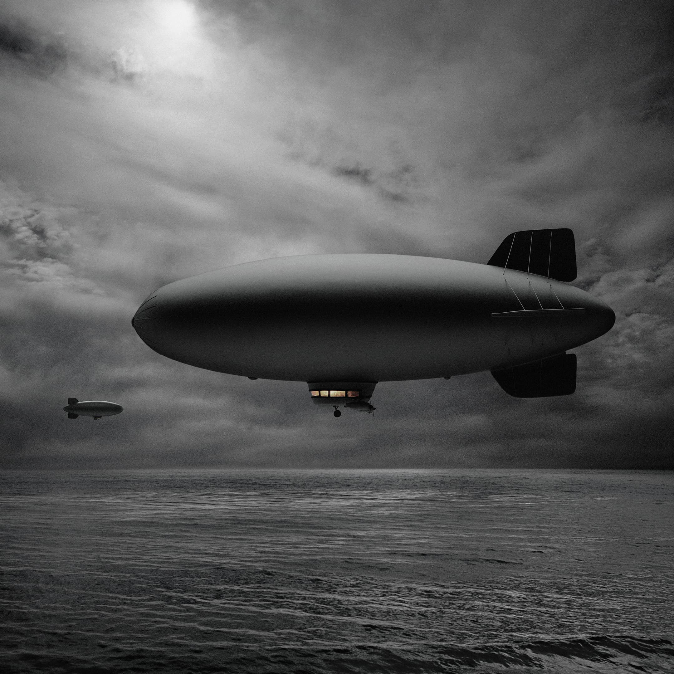 Moody black-and-white composite of two airships drifting low over a dark, choppy sea beneath a heavy clouded sky.